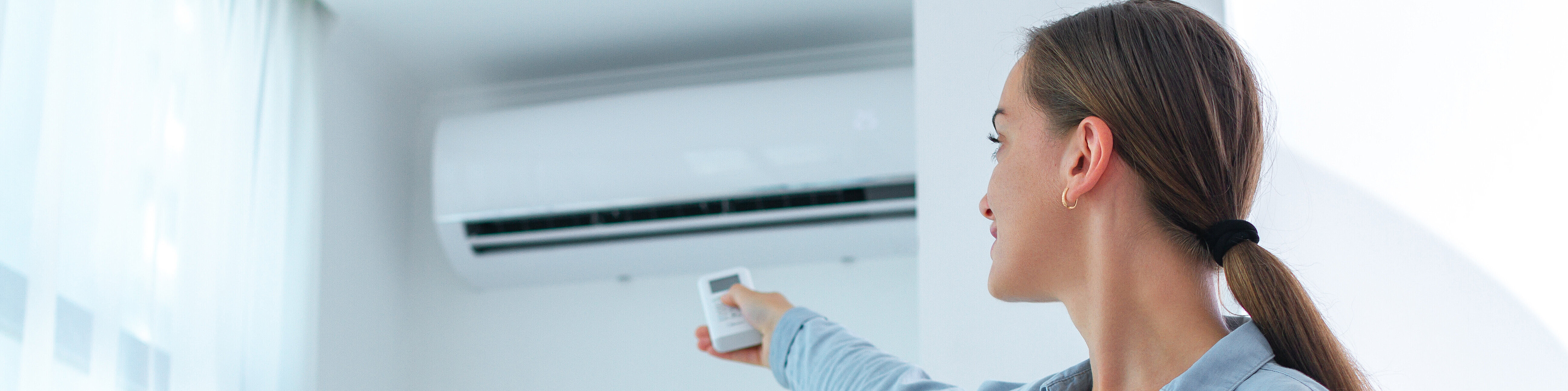 Eine Frau steht in einem Zimmer und bedient eine Klimaanlage mit einer Fernbedienung