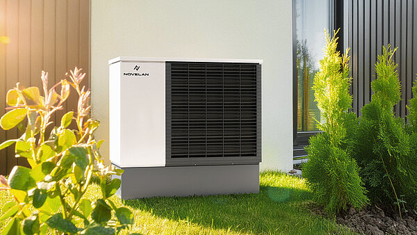 Wärmepumpe steht in einem Garten an einer Hausfassade